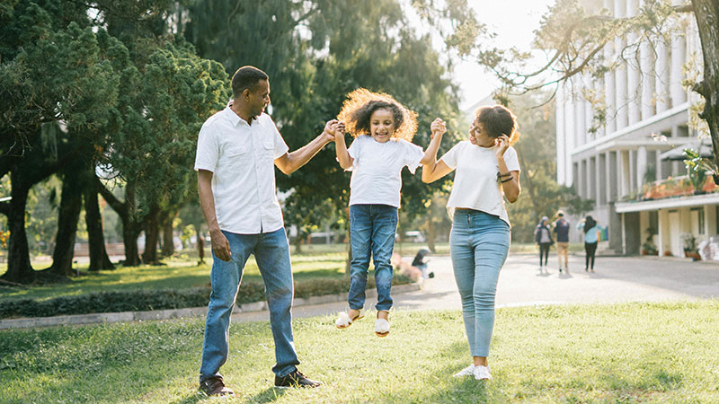 A joyful family moment in a park, with parents swinging their smiling child, highlighting supportive family interactions in overcoming childhood trauma